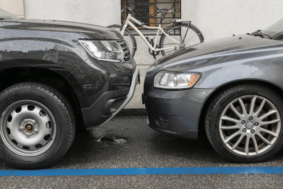 Two grey cars parked head to head at a curb with a white bike in background